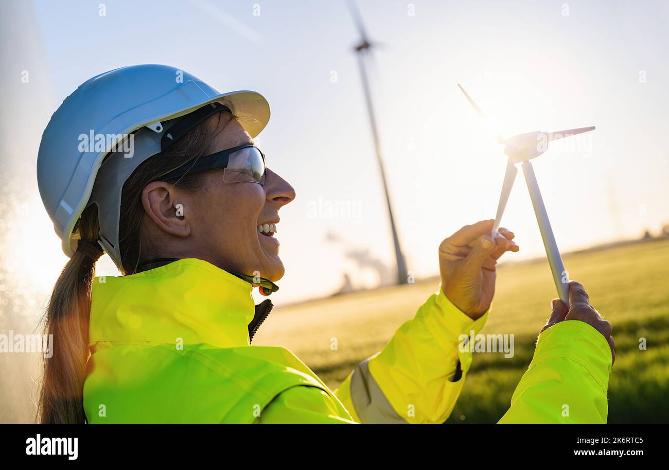 Sorridente ingegnere donna che tiene il modello di turbina eolica al tramonto. Nuova immagine del concetto di energia Foto Stock