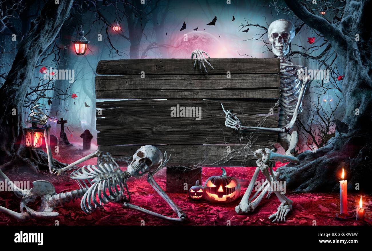 Carta di Halloween nella foresta con cartello in legno - cimitero di notte con zucche e scheletri Foto Stock