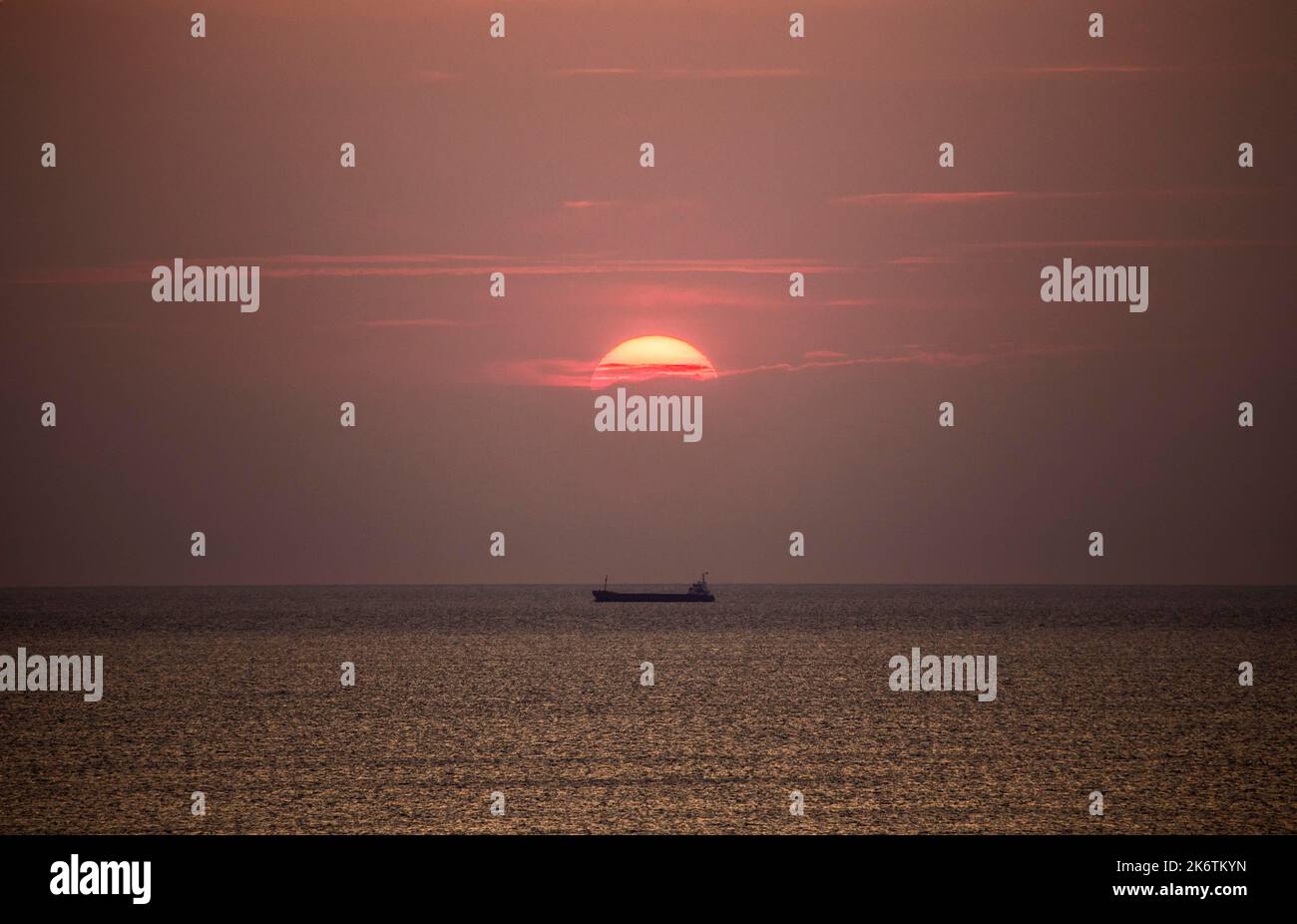 Nave da carico nel Mar Mediterraneo sotto il sole della sera, fotografata dalla spiaggia vicino Tarragona, Catalogna, Spagna Foto Stock