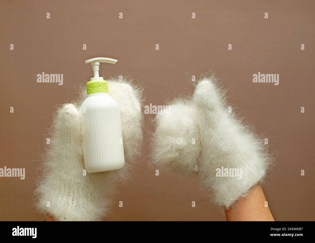 La bottiglia cosmetica della lozione idratante tiene le mani nei mitens. Foto Stock