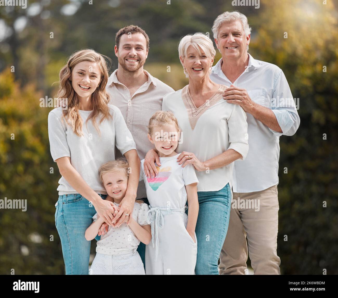 Famiglia felice in piedi fuori nel giardino. Un uomo e una donna sorridenti che si rilassano all'aperto con i loro figli e nipoti. Ragazze piccole che osservano Foto Stock