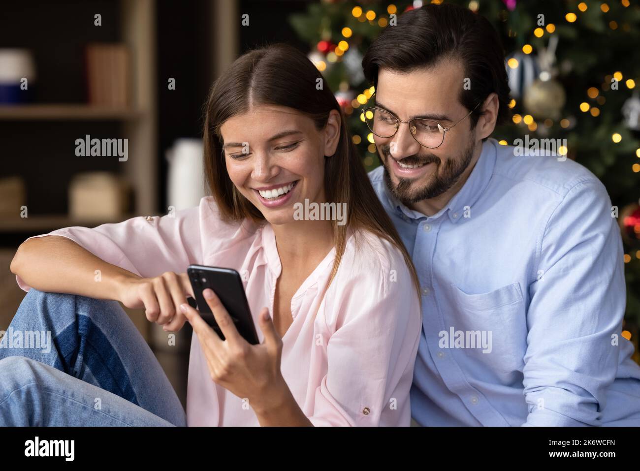 Giovane coppia allegra seduta insieme all'albero di Natale Foto Stock