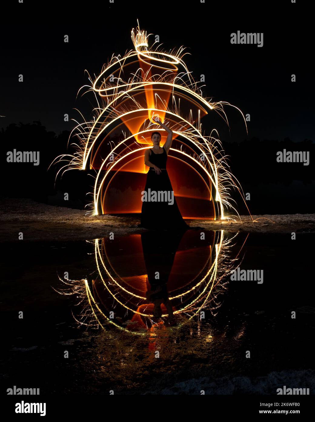 Donna in posa per fotografare con luci luminose al buio. Riflessione nell'acqua Foto Stock