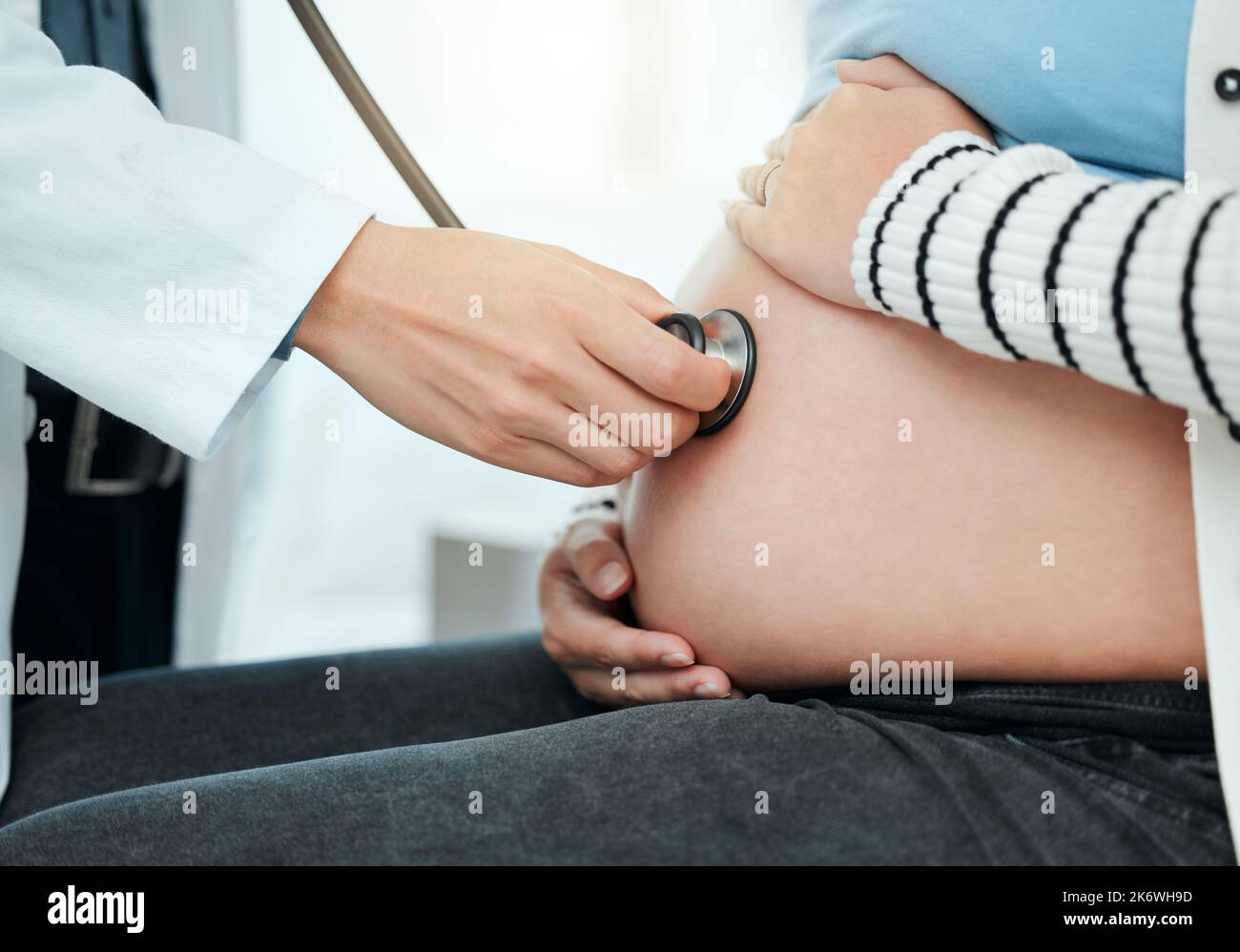 un medico non riconoscibile che usa uno stetoscopio sullo stomaco di una donna incinta durante un controllo. Foto Stock