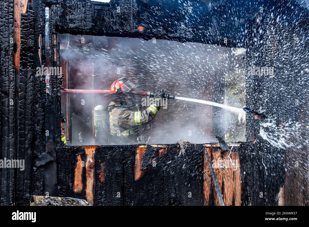 Un vigile del fuoco utilizza un tubo flessibile per estinguere i punti caldi e immergere le pareti come membri del Dipartimento dei vigili del fuoco di Springs, insieme al reciproco aiuto da parte del membro Foto Stock