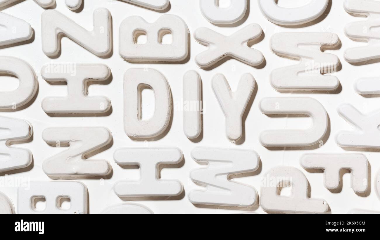 Abbreviazione DIY (fai da te) circondata da lettere stampate bianche casuali. Primo piano dell'iscrizione Foto Stock