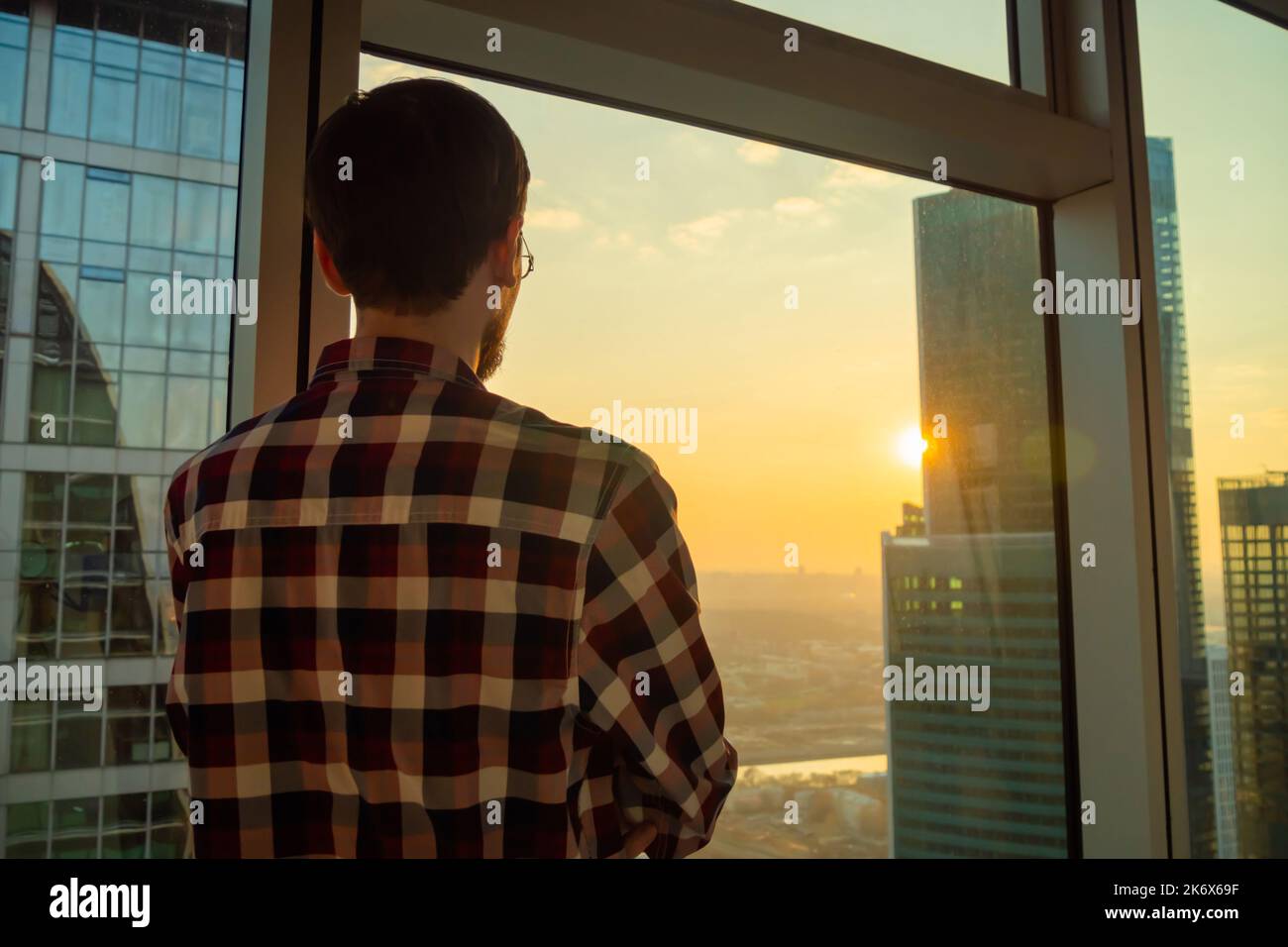 Vista posteriore dell'uomo che guarda il paesaggio urbano attraverso la finestra del grattacielo Foto Stock