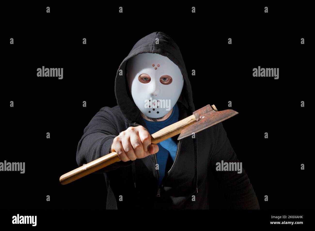 Uomo armato di un hatchet e che indossa una maschera da hockey e una felpa con cappuccio su sfondo nero. Foto Stock
