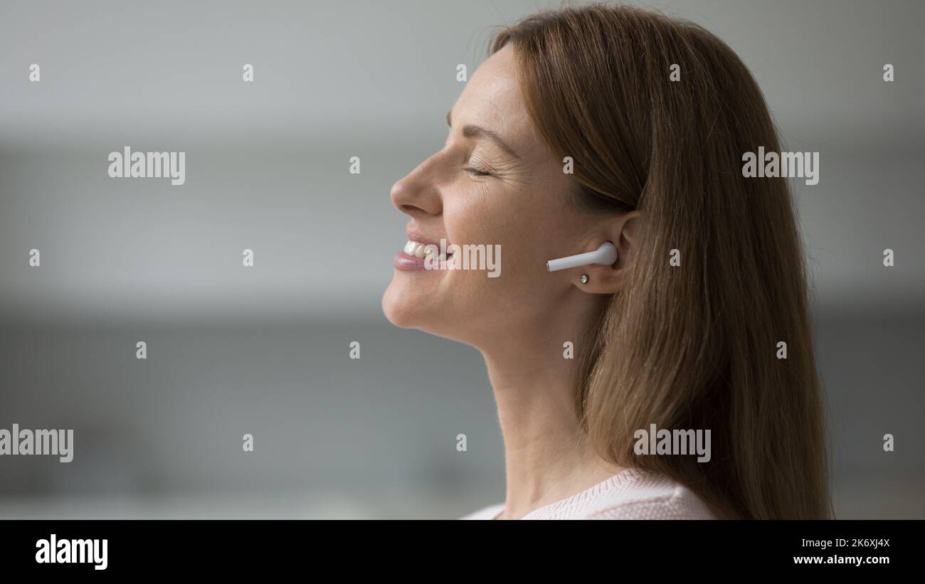 Profilo laterale viso di donna ascoltare la musica attraverso gli auricolari wireless Foto Stock