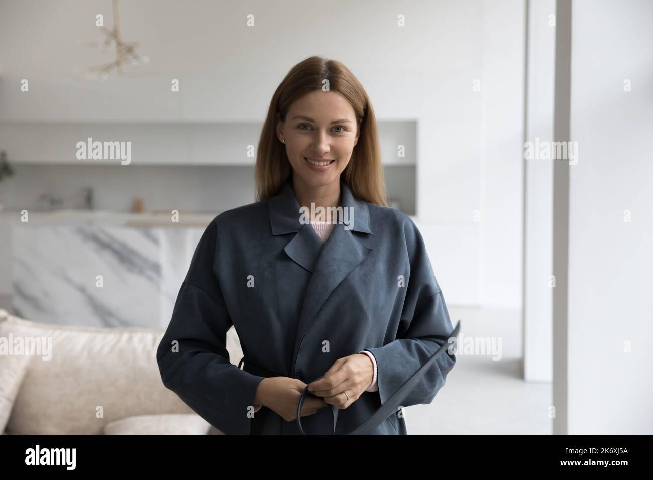 Donna che cerca un nuovo cappotto grigio sorridente fissando la fotocamera Foto Stock