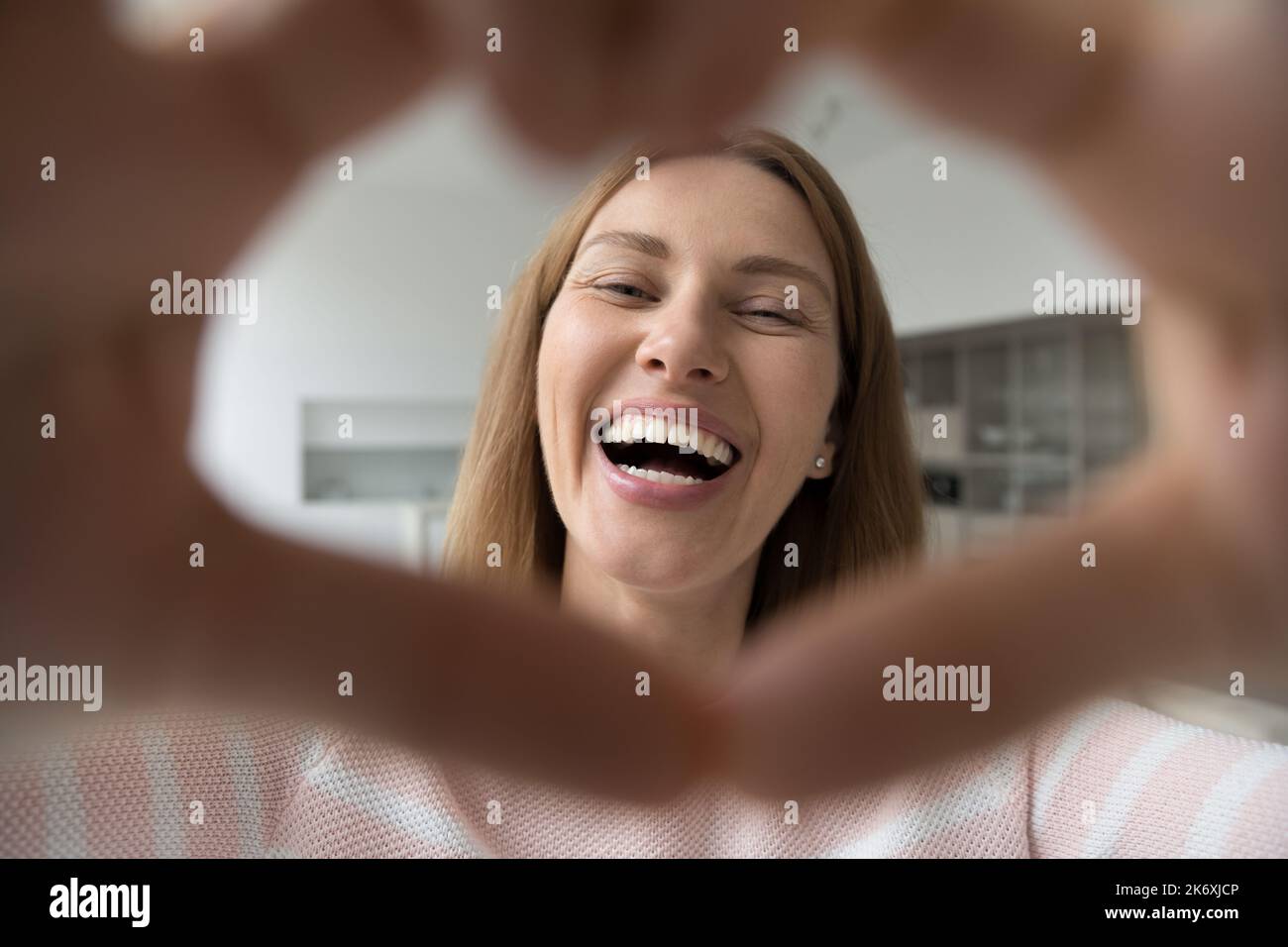 Donna felice che mostra il simbolo dell'amore, sorridere fissando la macchina fotografica Foto Stock