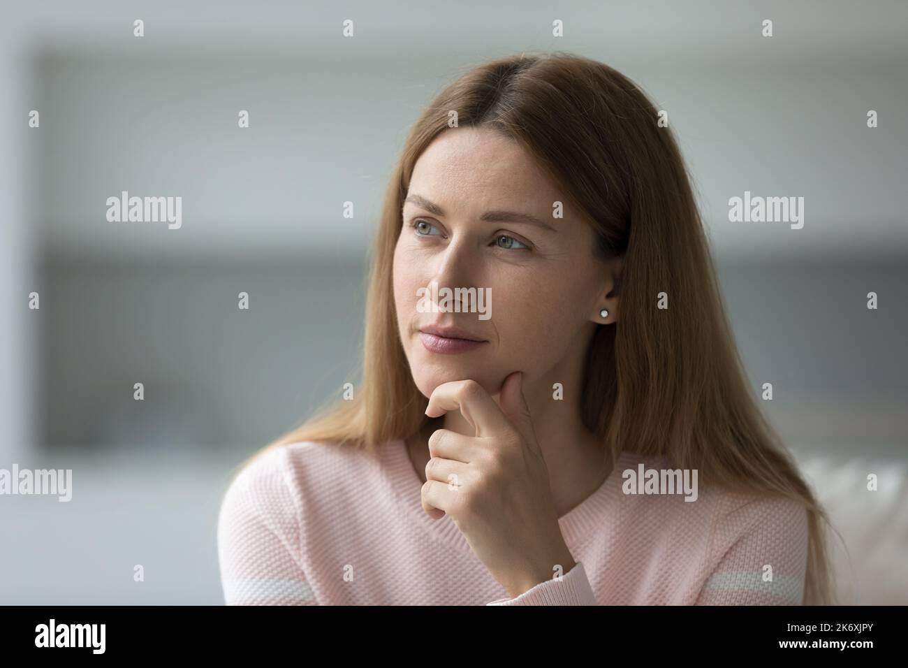 Bella donna premurosa guarda da parte seduto sul divano a casa Foto Stock