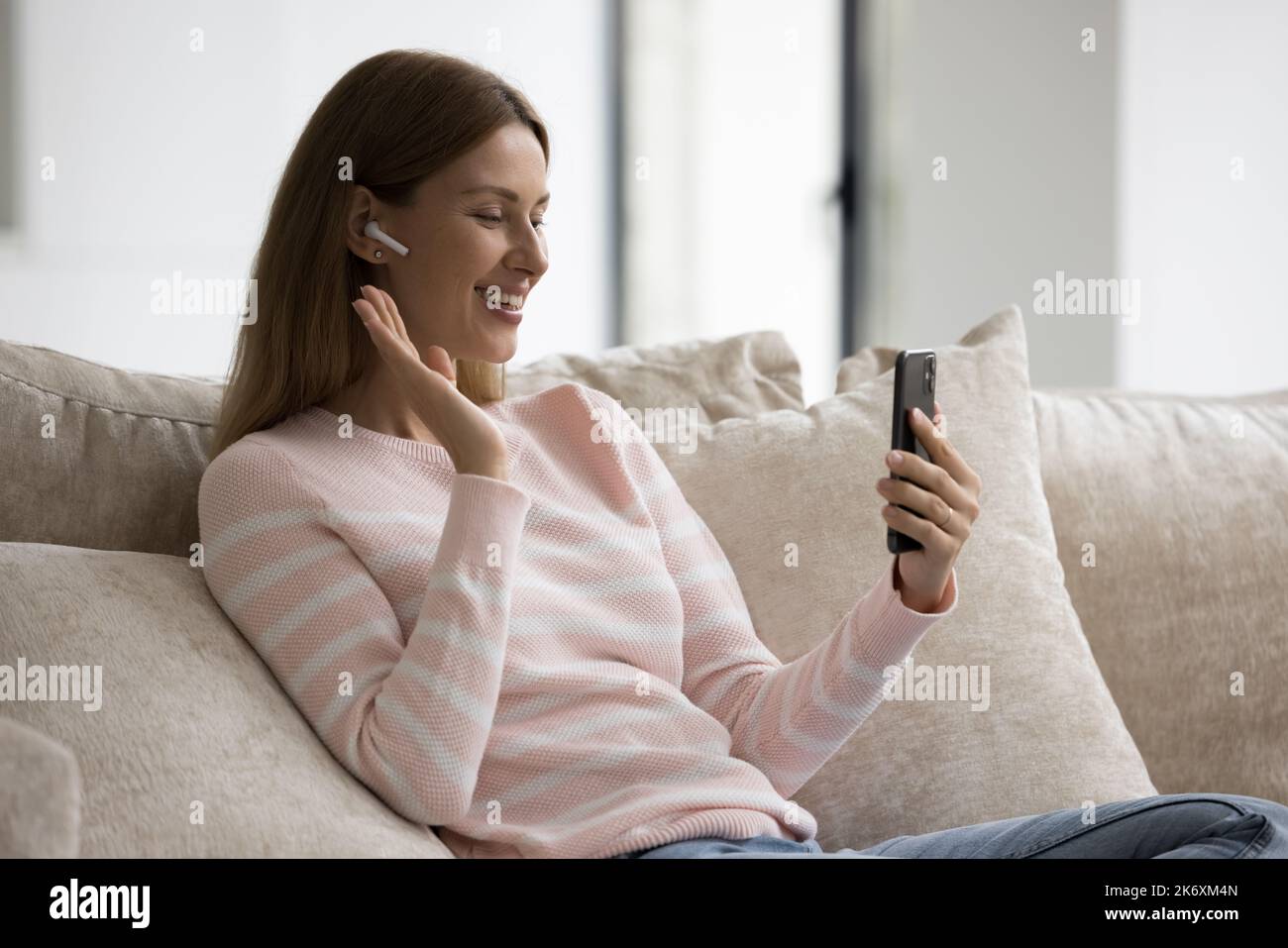 Donna indossare auricolari wireless rende la videochiamata utilizzando lo smartphone a casa Foto Stock
