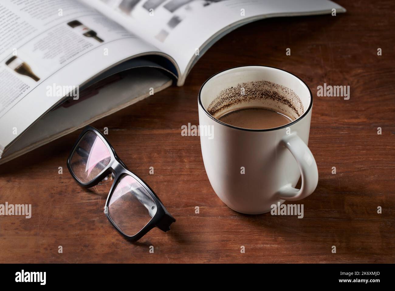 Un bicchiere di latte macinato, bicchieri da lettura e una rivista su un tavolo di legno Foto Stock