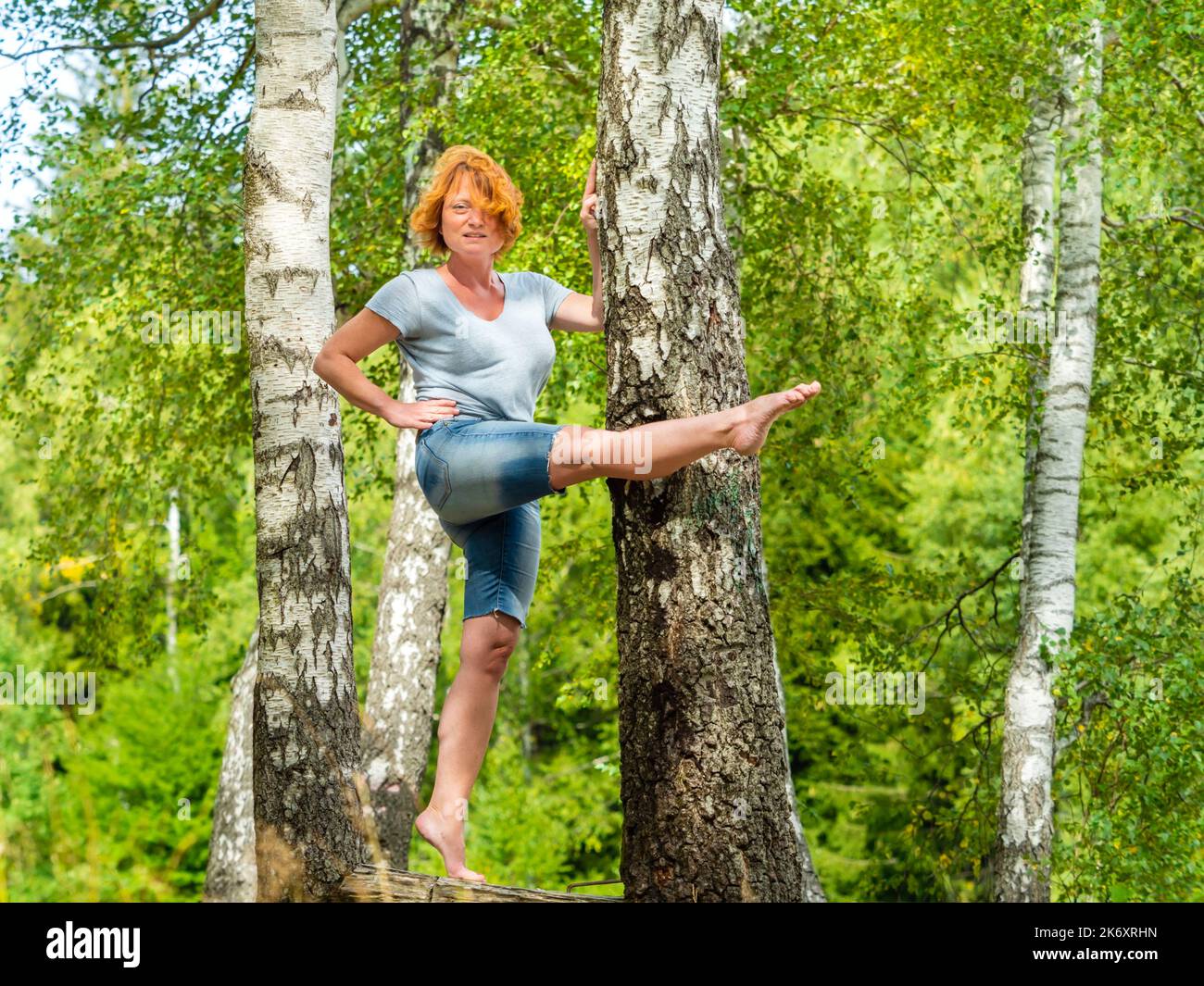 Donna matura in piedi su una gamba a piedi nudi nudi nel bosco verde foresta di bilanciamento e calci attivi spontanei Foto Stock
