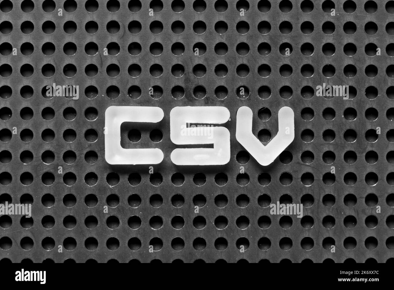 Lettera dell'alfabeto bianco in Word CSV (abbreviazione di computer System Validation o valori separati da virgole) su sfondo nero di pegboard Foto Stock