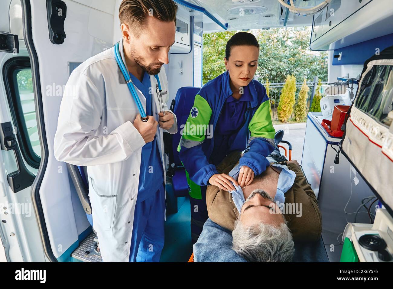 Paramedico in presenza di un medico che collega gli elettrodi ECG al torace del paziente maschio per fargli un esame elettrocardiografico all'interno dell'ambulanza. EMS Foto Stock