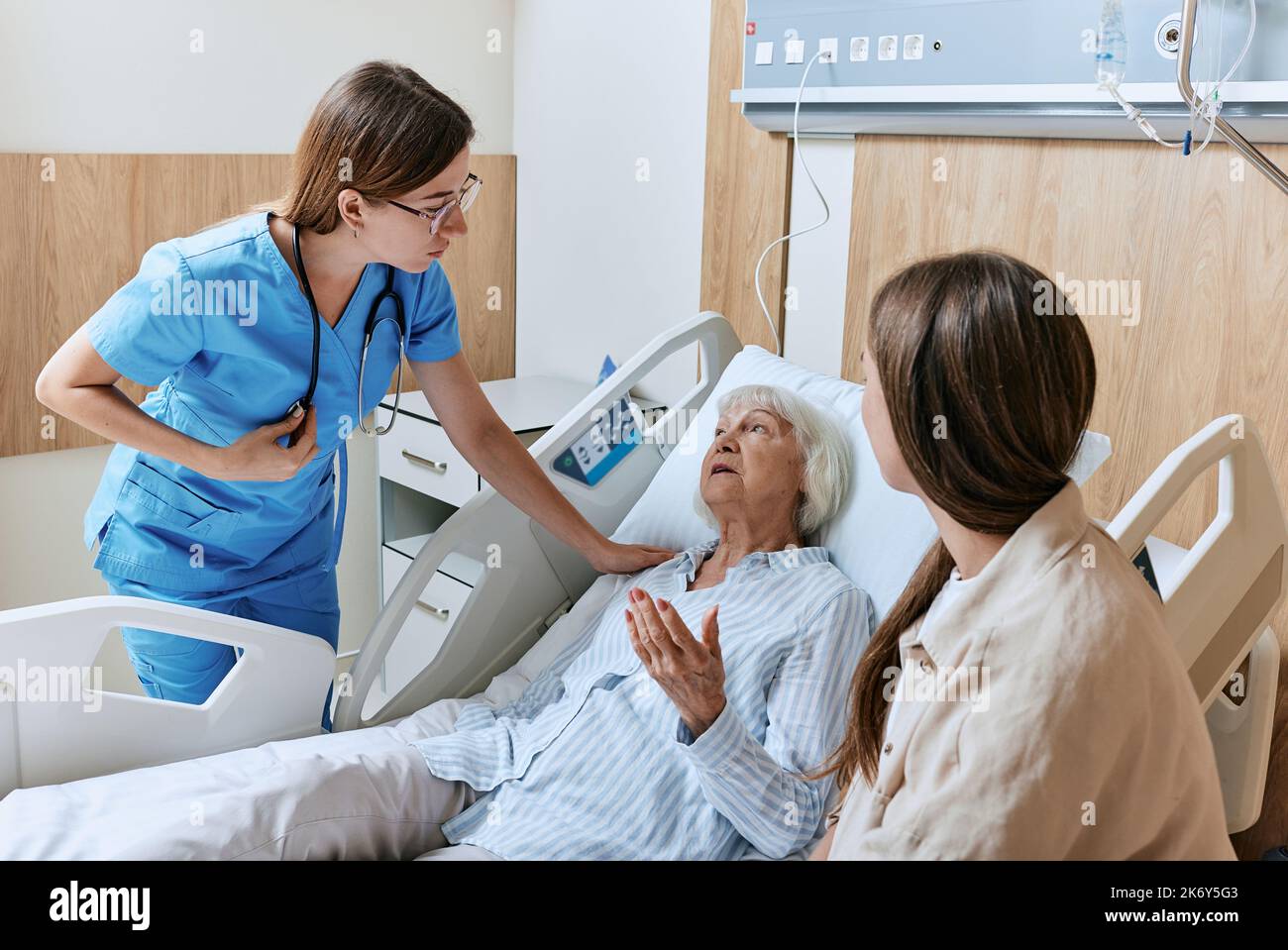 Infermiera che si occupa di pazienti anziani sdraiati nel letto del reparto ospedaliero, assistenza agli anziani. La figlia sostiene la paziente madre anziana durante il ciclo di infermiera di reparto Foto Stock