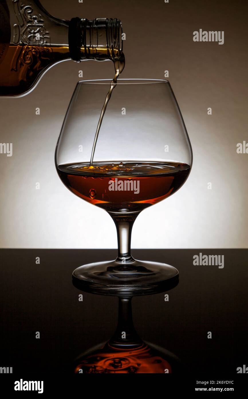 Versare un Cognac in un bicchiere di back-lite. Foto Stock