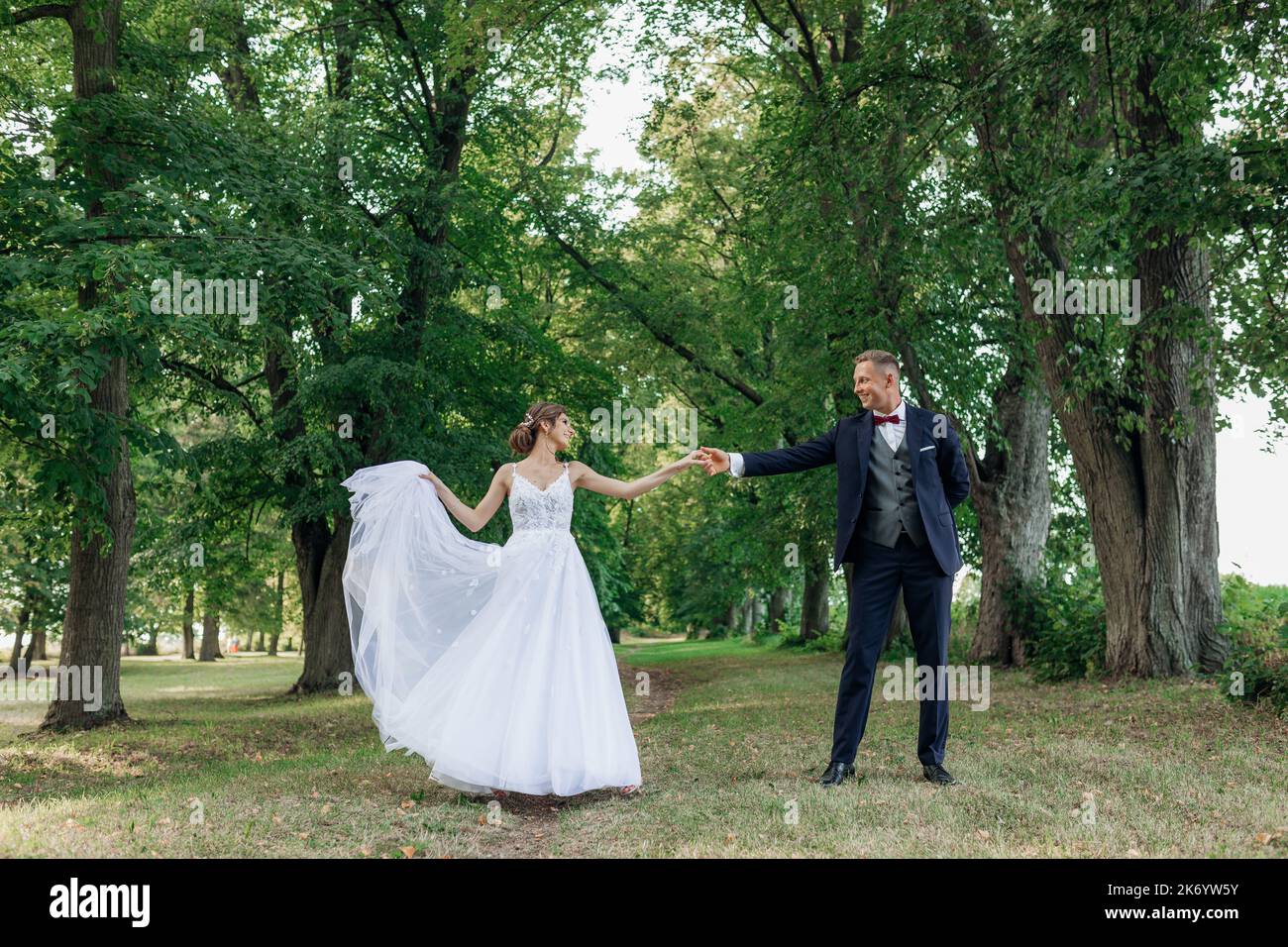 Giovane uomo sposo tenendo mano di giovane bella donna che si guarda l'un l'altro, sposa sollevamento bordo di vestito. Matrimonio, ballo. Foto Stock