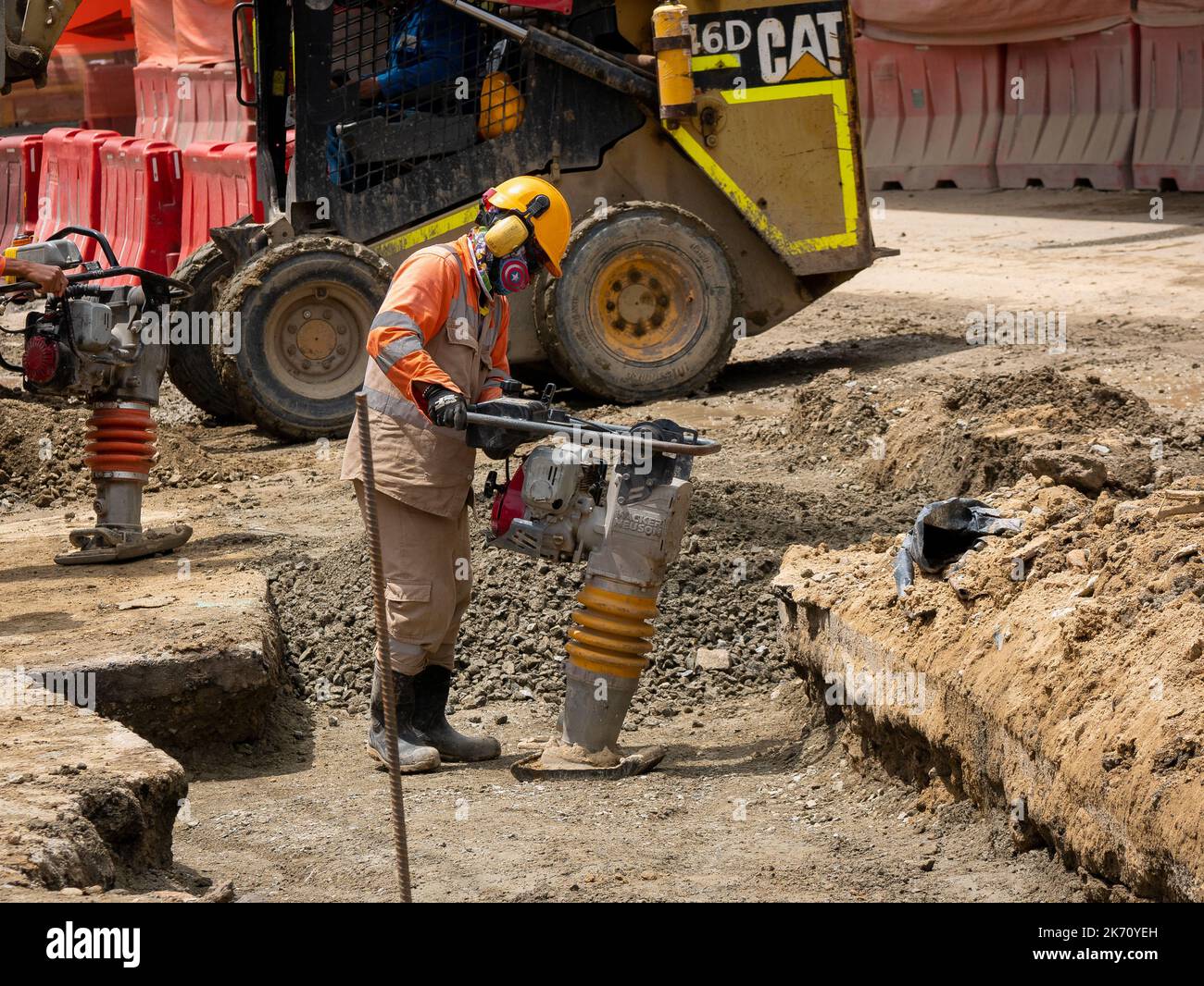 Medellin, Antioquia, Colombia - Giugno 2 2022: Uomo colombiano che lavora in costruzione con un Rammer di manomissione elettrica che indossa una uniforme arancione di sicurezza AN Foto Stock