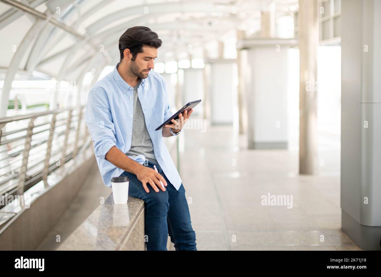 Il giovane uomo che usa un tablet per lavorare fuori ufficio. L'uomo che indossa un panno casual e si sente rilassante e felice. Foto Stock