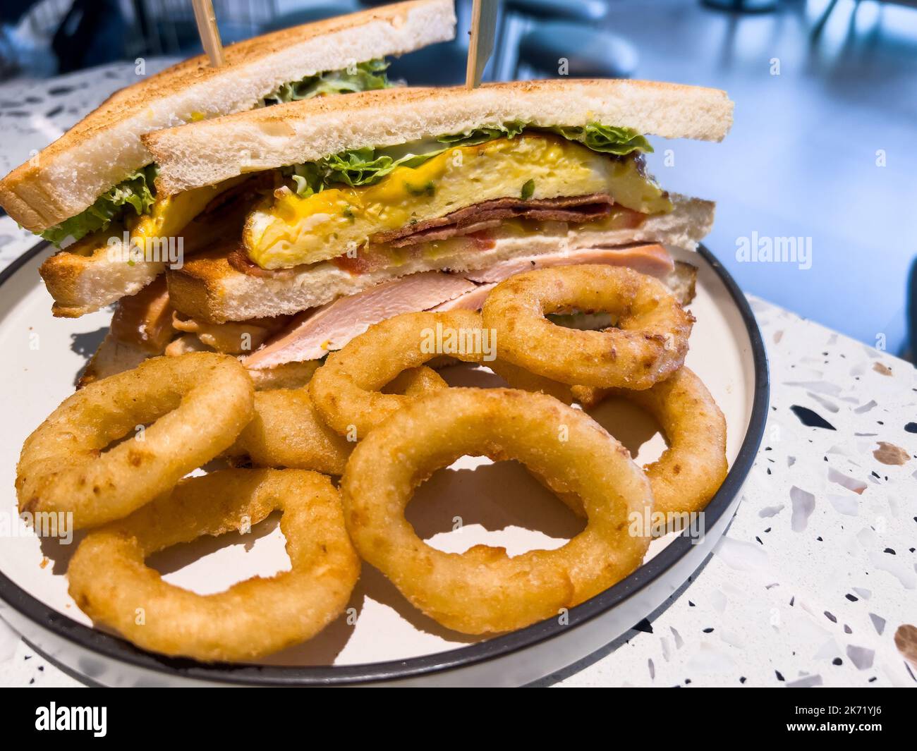 All'interno di un bar, ordinato un club sandwich con pollo marinato, pancetta di tacchino, prosciutto, uova strapazzate e anelli di cipolla come lato. Foto Stock