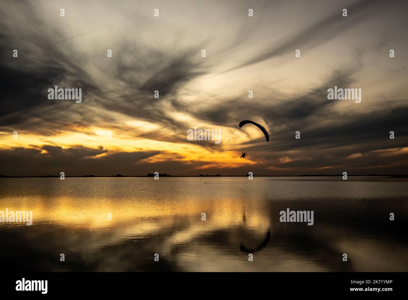 Paesaggio lagunare durante il tramonto. Un parapendio motorizzato si avvicina mostrando la sua silhouette contro la luce. Foto Stock