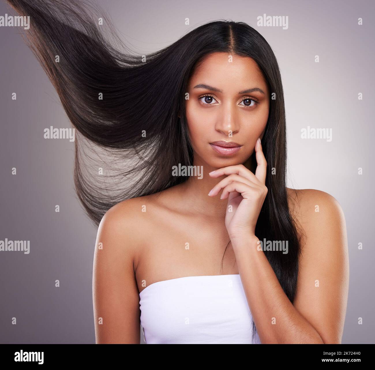 I miei capelli sono meravigliosi, lo so. una giovane donna attraente che si alza da sola e guarda contemplativa mentre si posa in studio. Foto Stock