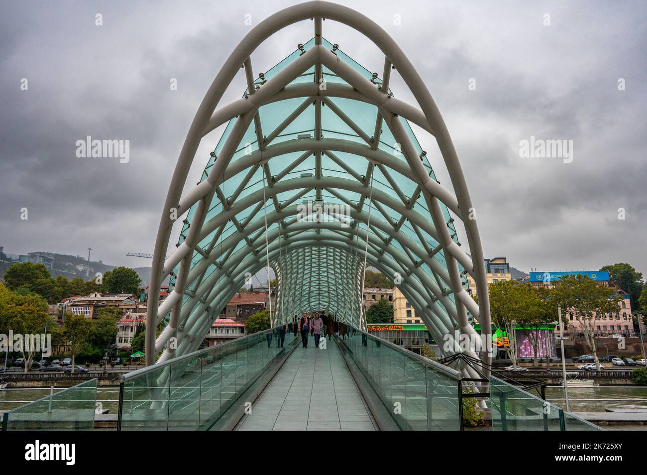 Il Ponte della Pace è un ponte pedonale a forma di arco, una costruzione in acciaio e vetro che attraversa il fiume Kura a Tbilisi Foto Stock