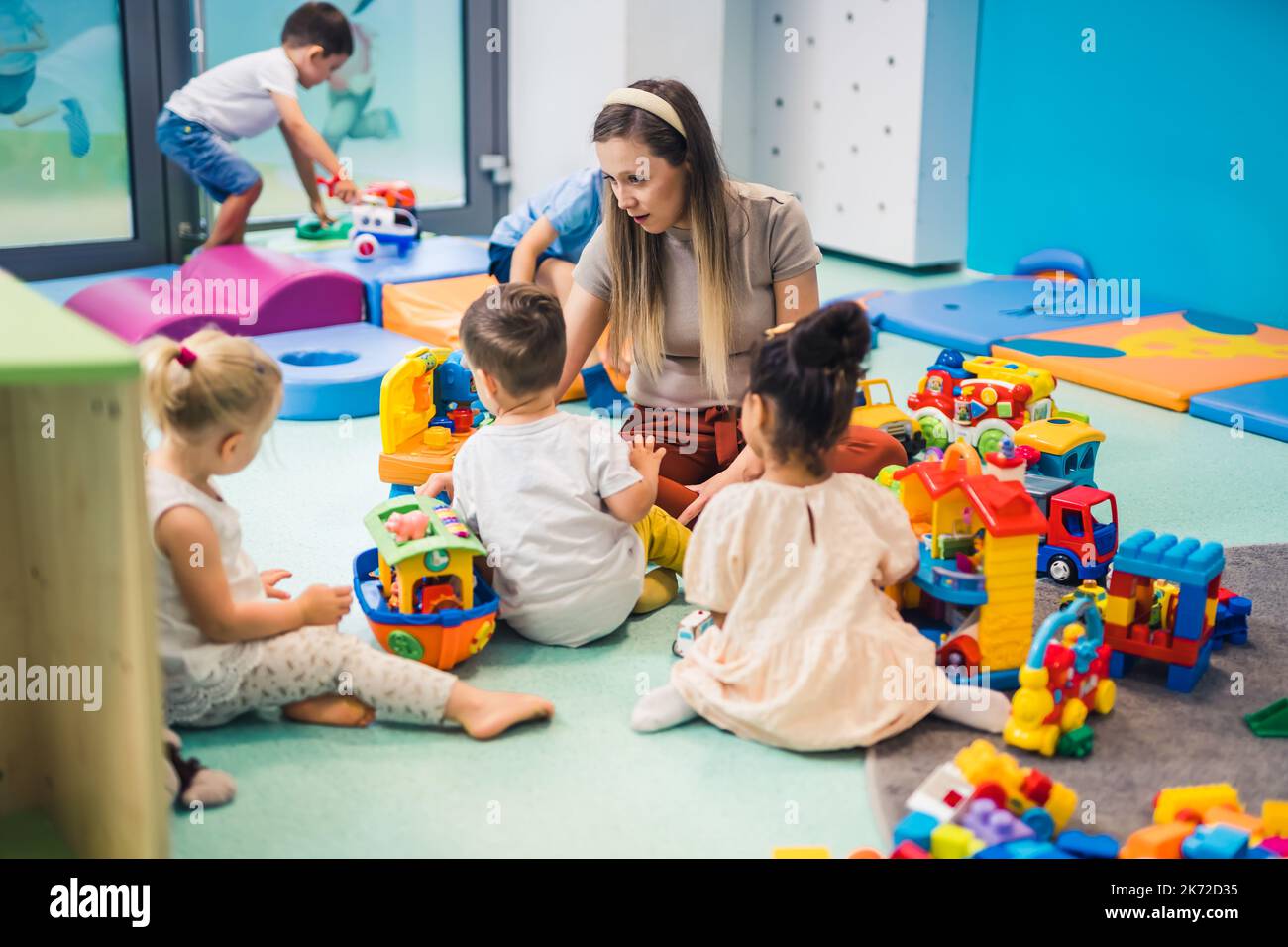 i presciolieri seduti sul pavimento circondavano un sacco di giocattoli e si divertono con il loro insegnante, asilo nido. Foto di alta qualità Foto Stock