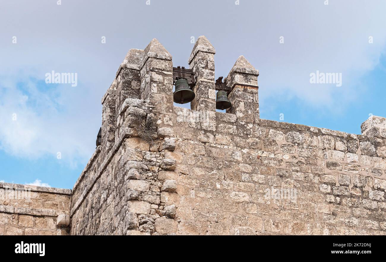 Due antiche campane di bronzo su un muro di pietra calcarea in uno storico monastero cristiano a Beit Shemesh vicino a Gerusalemme in Israele con un cielo nuvoloso Foto Stock