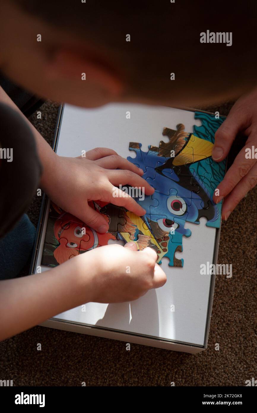 Primo piano di un giovane ragazzo che assembla un puzzle colorato sul tappeto con la madre vista dall'alto Foto Stock