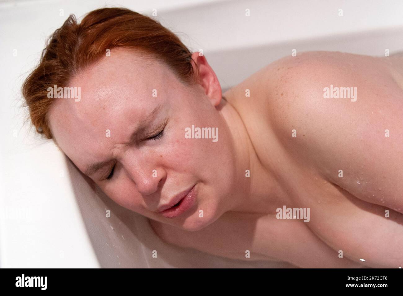 Una donna incinta con dolori di contrazione sdraiata al suo fianco in un bagno caldo a casa durante le prime fasi del travaglio Foto Stock
