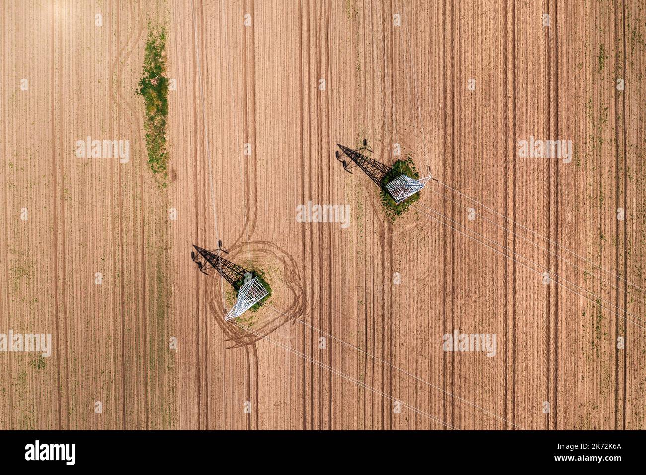 Due torri di trasmissione a traliccio elettrico e linee elettriche che gettano ombre sul campo coltivato, drone pov direttamente sopra Foto Stock