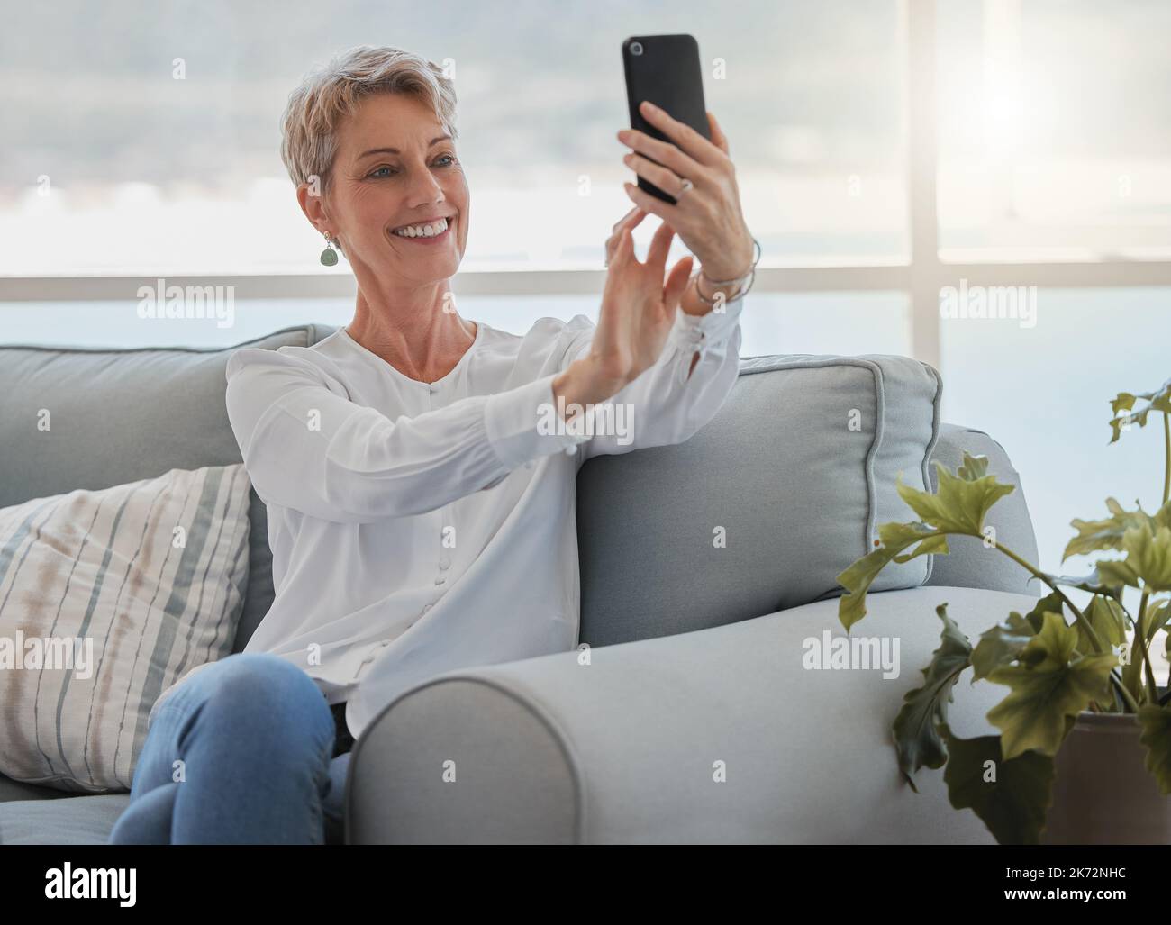 Vivere la sua vita migliore. una donna anziana attraente che prende selfie mentre si rilassa nel suo salotto a casa. Foto Stock