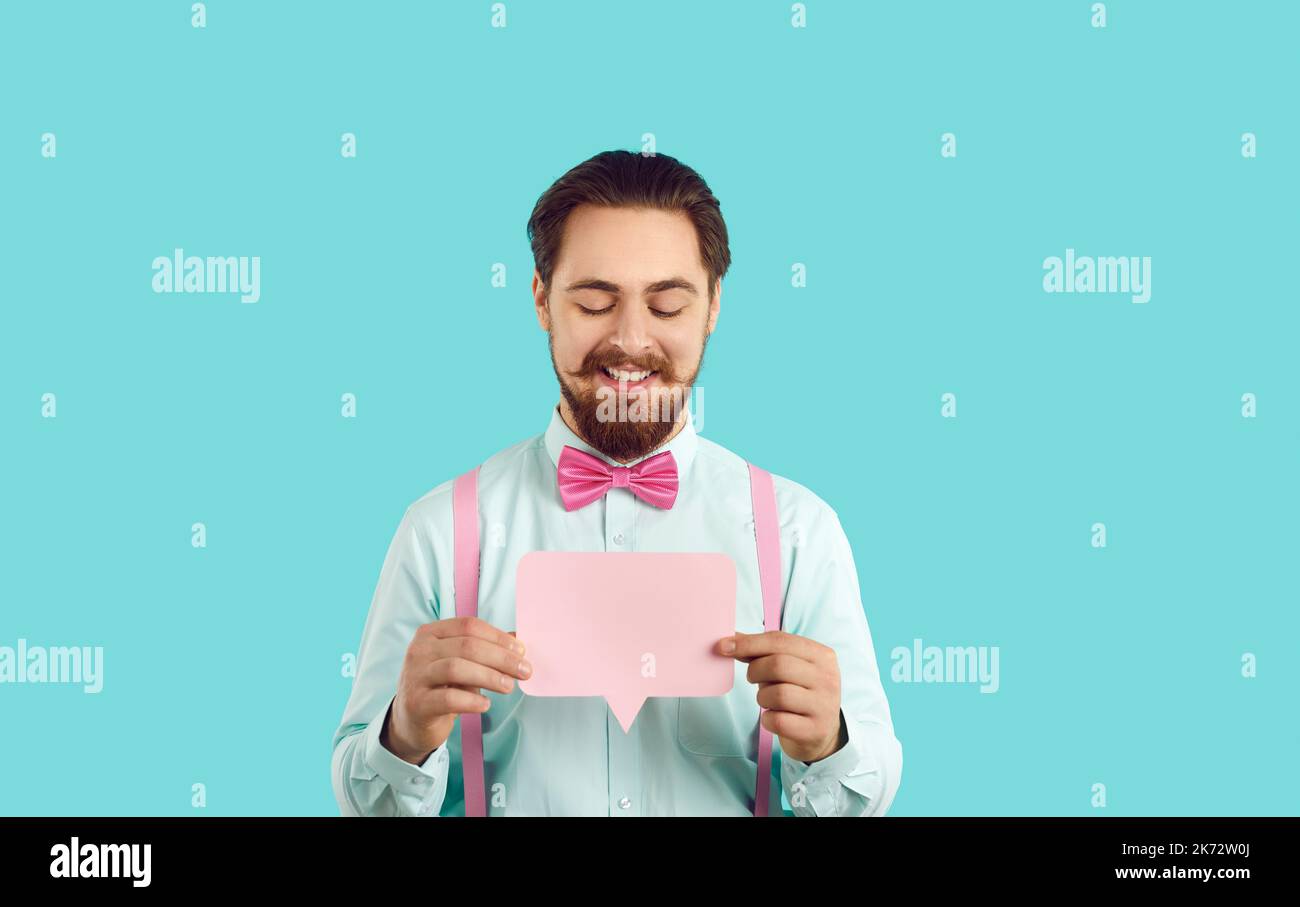 Allegro uomo elegante hipster che tiene vuota bolla di linguaggio rosa su sfondo turchese. Foto Stock