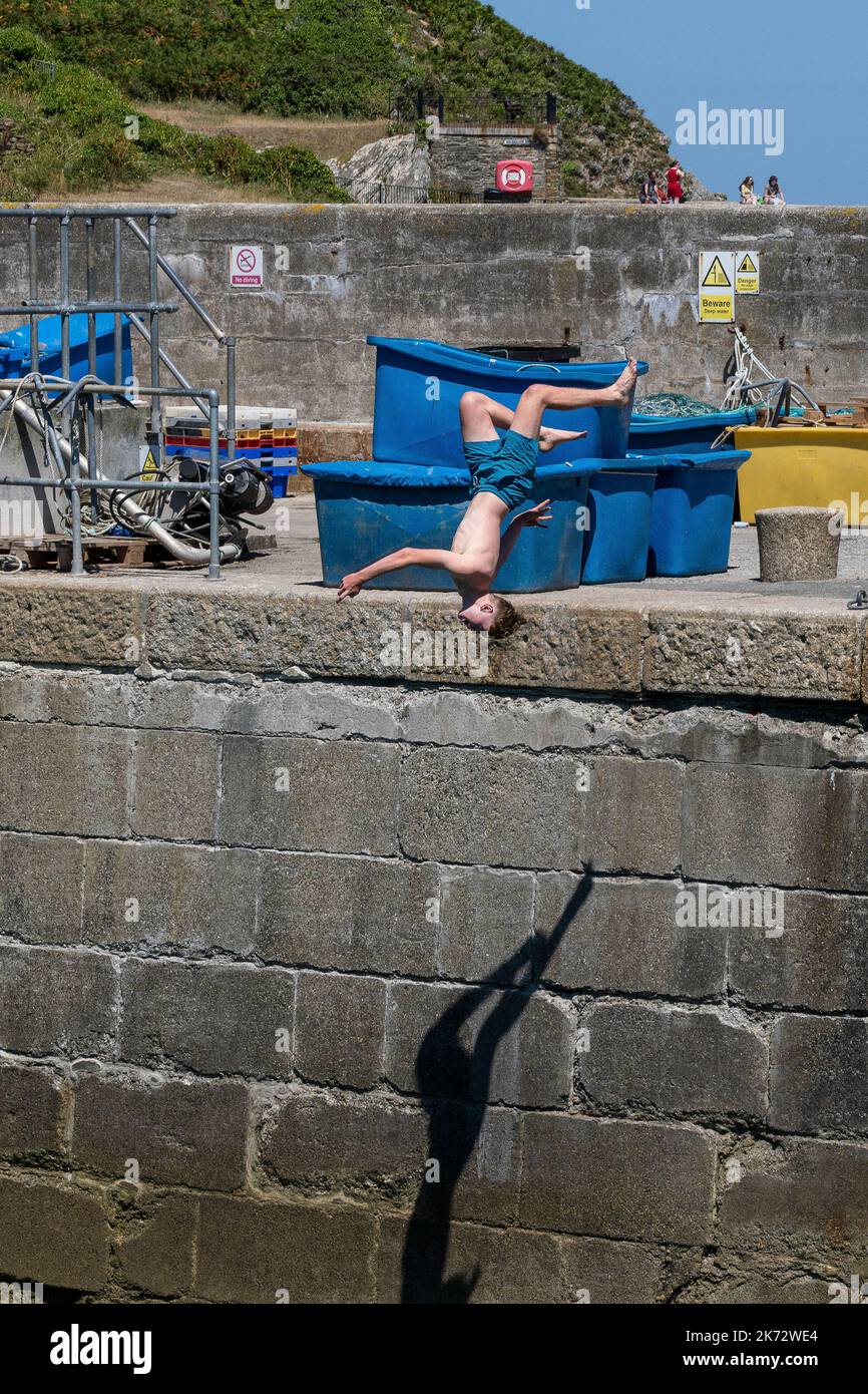 Un giovane adolescente maschio che fa un salto acrobatico nel mare a Newquay Harbour in Cornovaglia in Inghilterra nel Regno Unito. Foto Stock