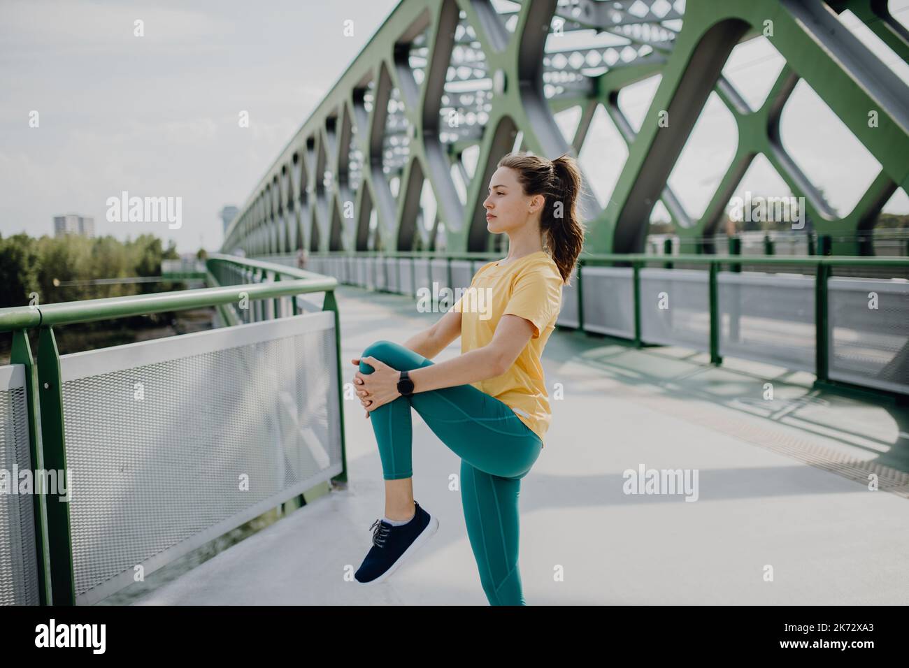 Giovane donna che fa stretching in città, preparandosi per la corsa, stile di vita sano e concetto di sport. Foto Stock