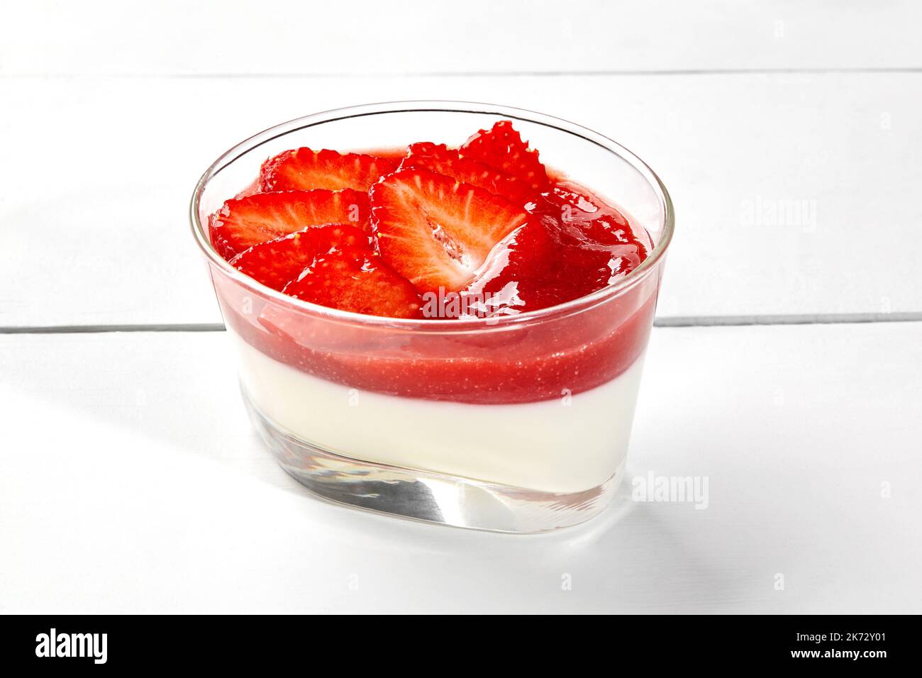 Panna cotta cremosa con coulis di fragole e rabarbaro e frutti di bosco freschi in vetro su tavolo di legno bianco Foto Stock