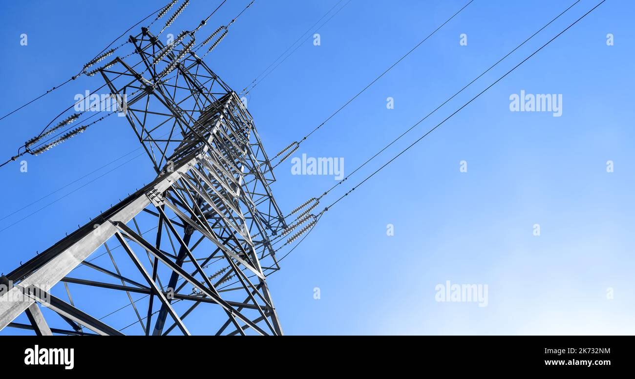 Struttura in acciaio Power Pylon con cavi ad alta tensione contro il cielo e il sole blu Foto Stock
