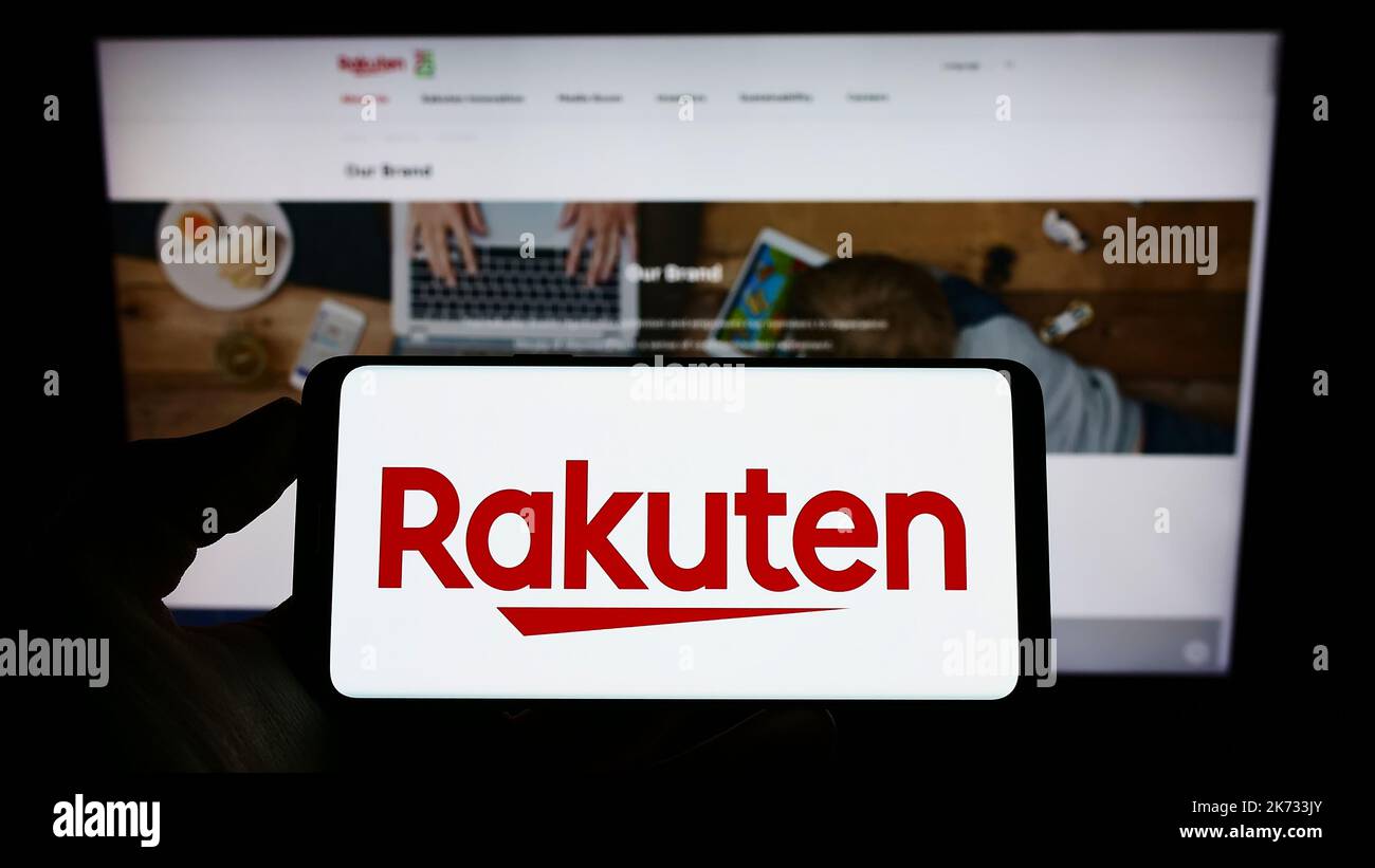 Persona che tiene il cellulare con il logo della società giapponese di e-commerce Rakuten Group Inc. Sullo schermo di fronte al sito web. Messa a fuoco sul display del telefono. Foto Stock