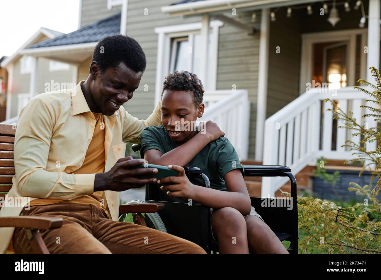 Ritratto di un ragazzo sorridente che guarda lo schermo dello smartphone mentre passa il tempo con il padre all'aperto Foto Stock
