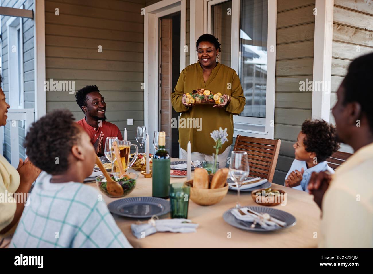 Ritratto di donna nera sorridente che porta cibo a tavola mentre si gode la famiglia riunione all'aperto Foto Stock