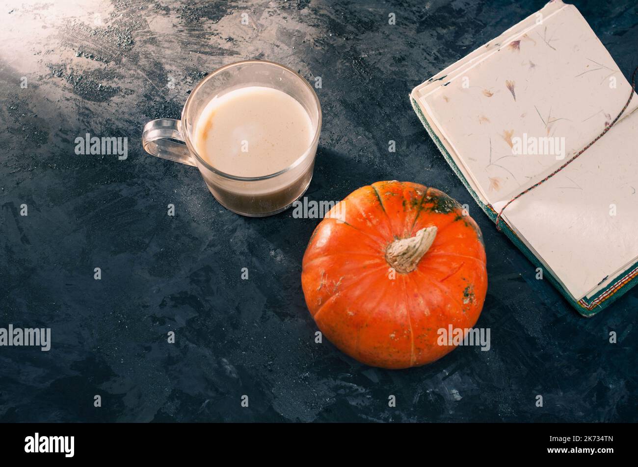 Una zucca di zucca e un caffè latte preparato con soia di avena a base di piante o latte di mandorla con taccuino vuoto al tavolo sul nero scuro b Foto Stock