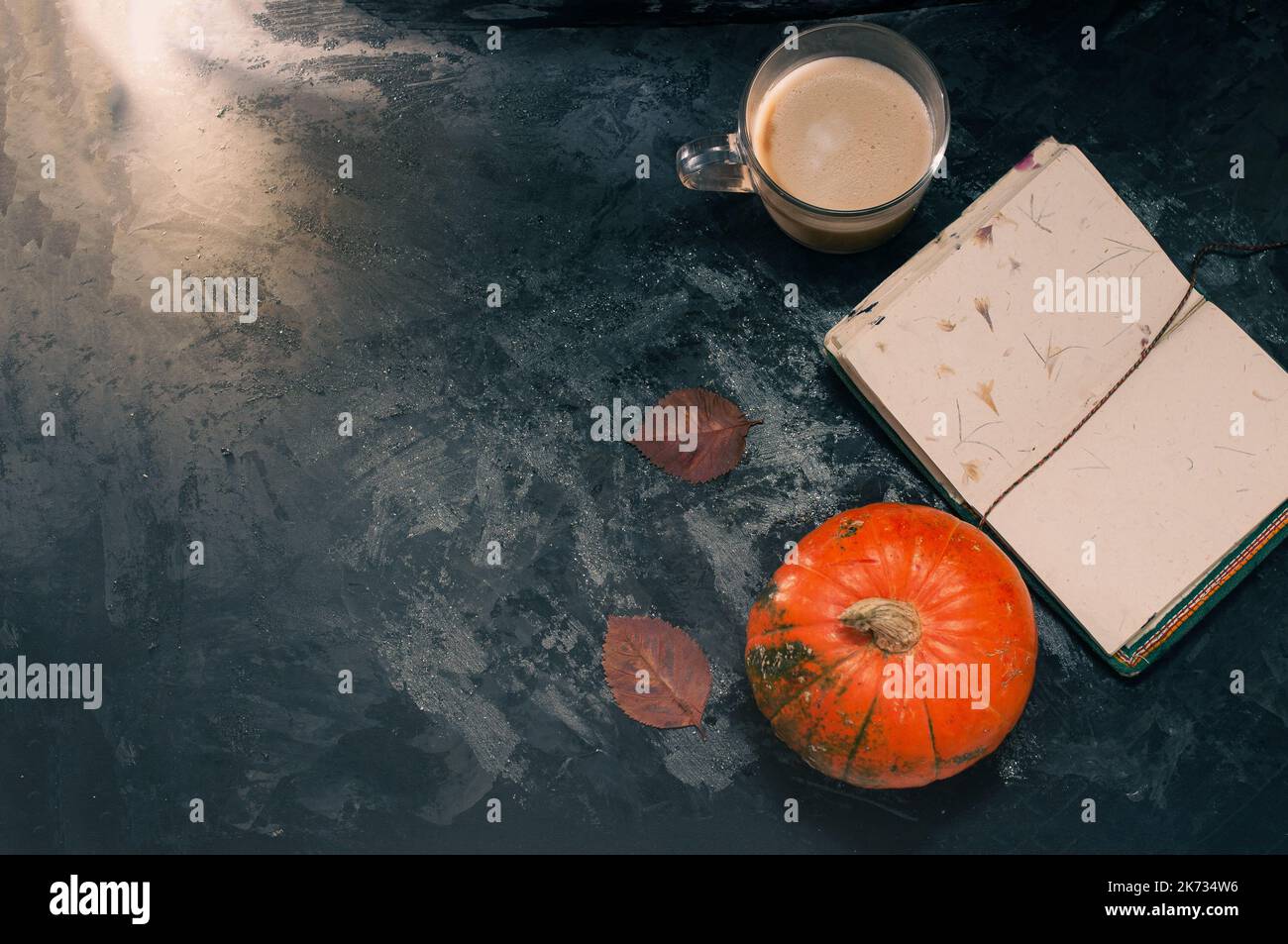 Una zucca di zucca e un caffè latte preparato con soia di avena a base di piante o latte di mandorla con taccuino vuoto al tavolo sul nero scuro b Foto Stock