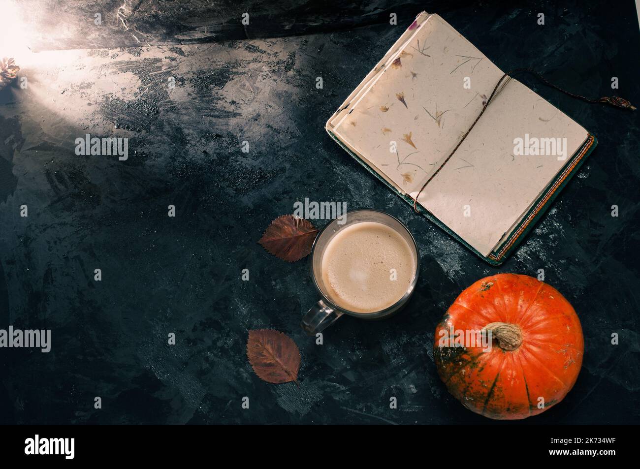 Una zucca di zucca e un caffè latte preparato con soia di avena a base di piante o latte di mandorla con taccuino vuoto al tavolo sul nero scuro b Foto Stock