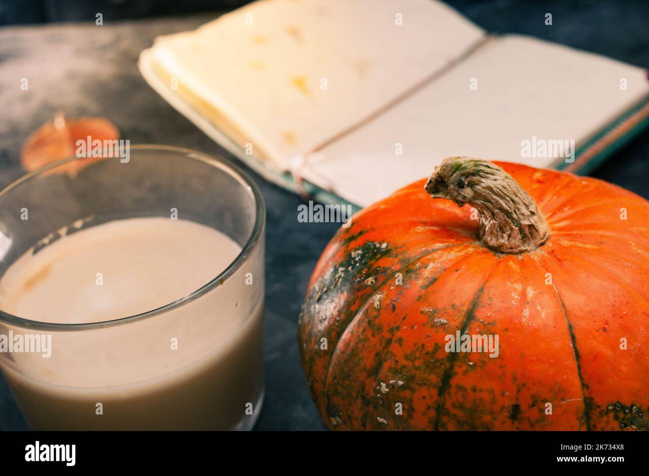 Una zucca di zucca e un caffè latte preparato con soia di avena a base di piante o latte di mandorla con taccuino vuoto al tavolo sul nero scuro b Foto Stock