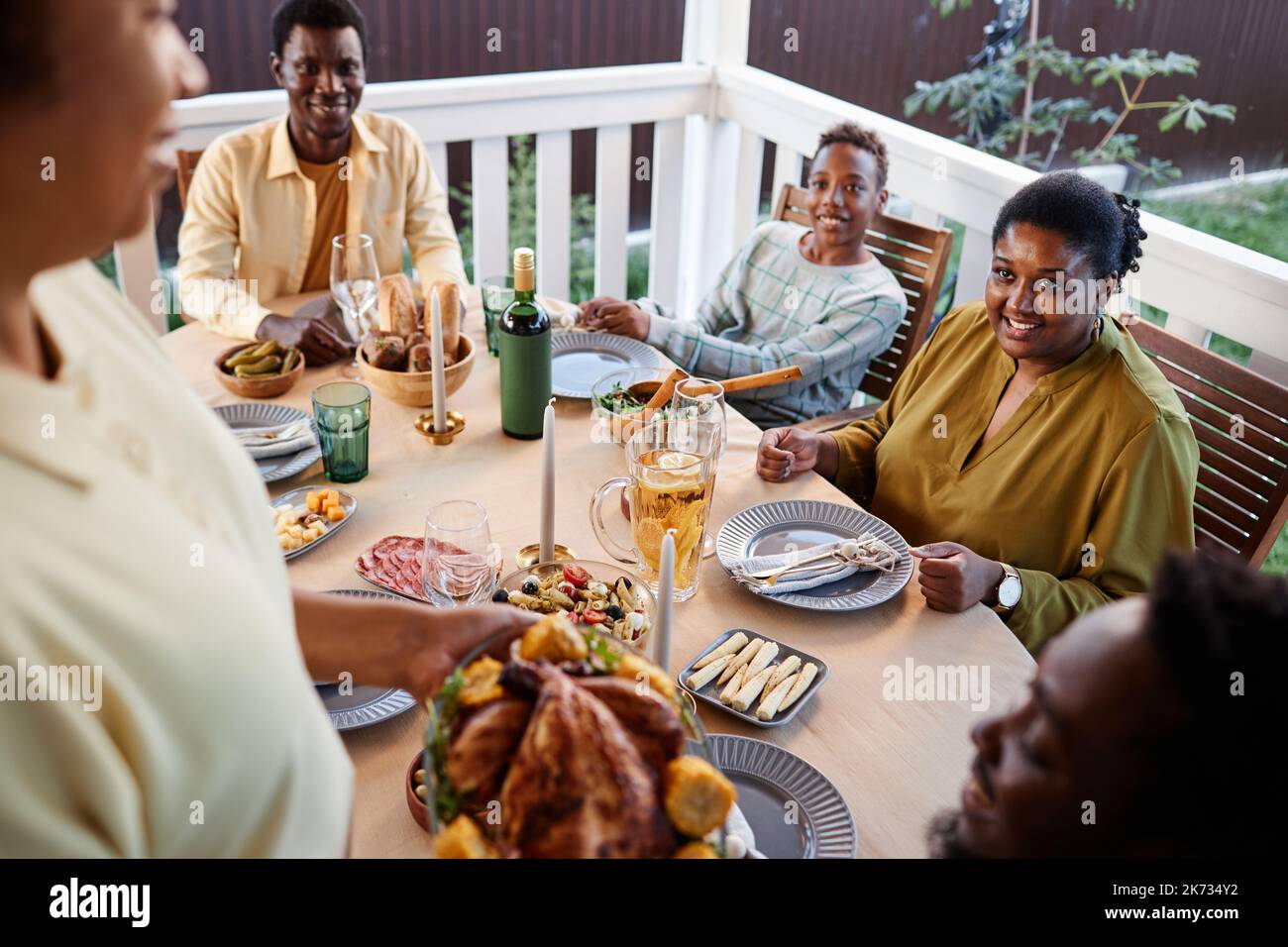 Vista ad alto angolo della donna che porta piatti di pollo fatti in casa al tavolo durante la cena in famiglia all'aperto Foto Stock