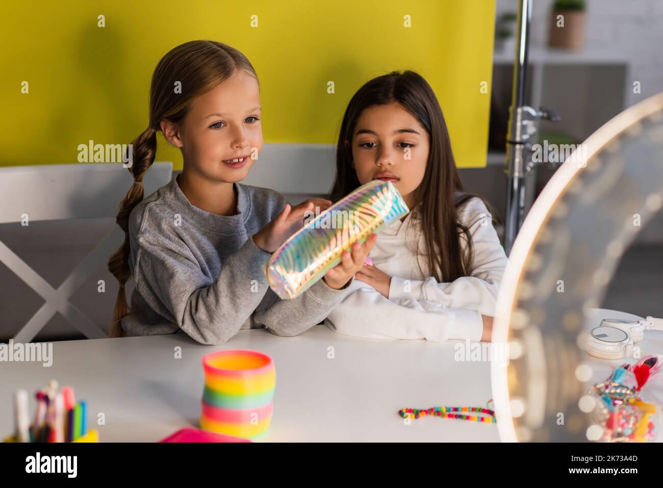pre blogger dimostrando matita case vicino amico e cerchio lampada in primo piano sfocato Foto Stock